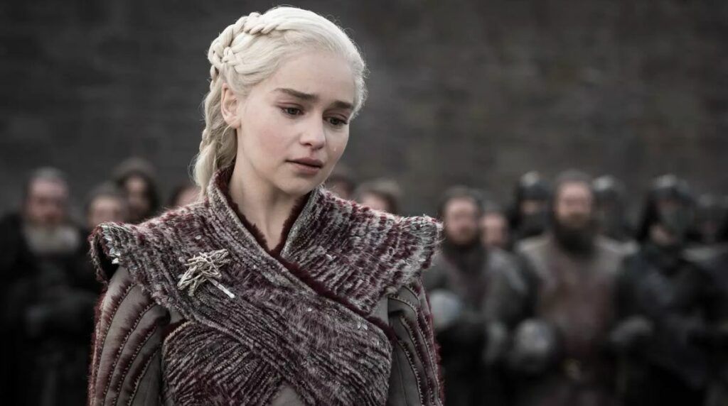 Emilia Clarke dans la série Game of Thrones coiffée de sa perruque blonde avec ses tresses et regardant par terre