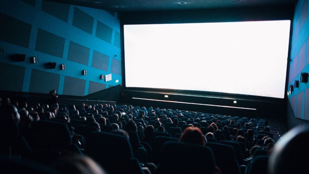 Une image avec une salle de cinéma avec un écran blanc et des spectateurs 